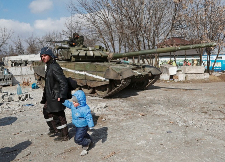Un residente local camina con un niño frente a un tanque de tropas prorrusas. 