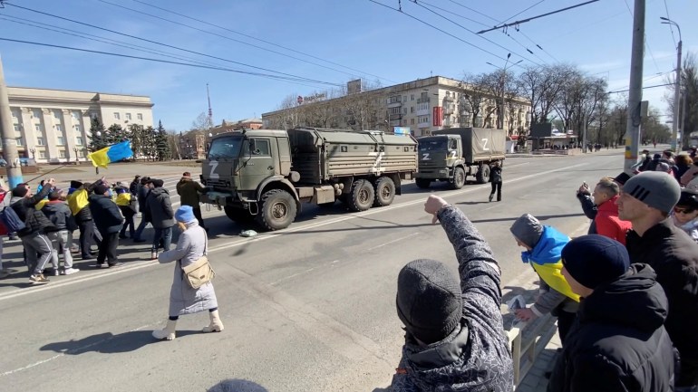 Un manifestante gesticula mientras otros, portando banderas ucranianas, corean "volver a su casa" y marchan hacia vehículos militares rusos durante una manifestación pro-ucraniana en medio de la invasión rusa, en Kherson, Ucrania, el 20 de marzo de 2022 