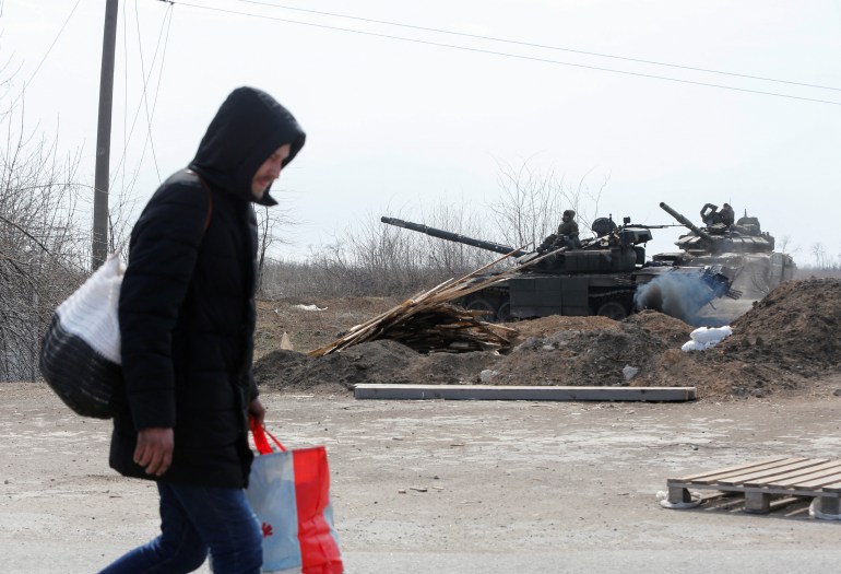 Un hombre lleva sus pertenencias frente a un tanque ruso