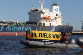 Greenpeace activists hold a banner that reads 'Oil fuels war' in a boat alongside an oil tanker
