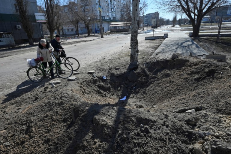 Local residents stand next to a shell crater at an empty street, amid Russia's invasion of Ukraine, in Sievierodonetsk, Luhansk region.