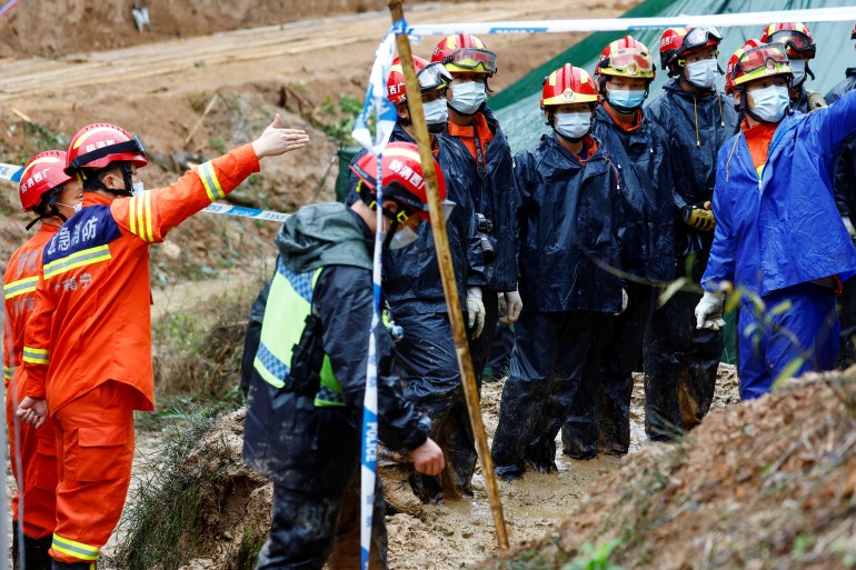 Rescue teams in red and blue uniforms stand in the mud as they search the China Eastern plane crash site