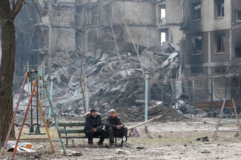Local residents sit on a bench near an apartment building destroyed in the course of Ukraine-Russia conflict.