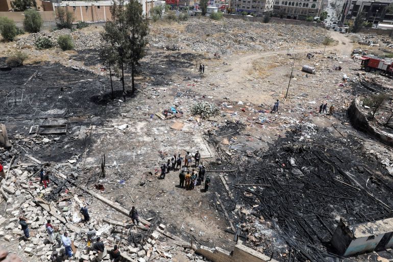 People stand amid rubble and blackened earth at the site of Saudi-led air attacks in Sanaa