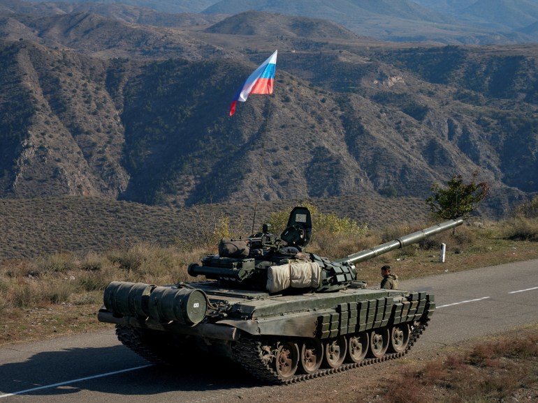A service member of the Russian peacekeeping troops stands next to a tank near the border with Armenia