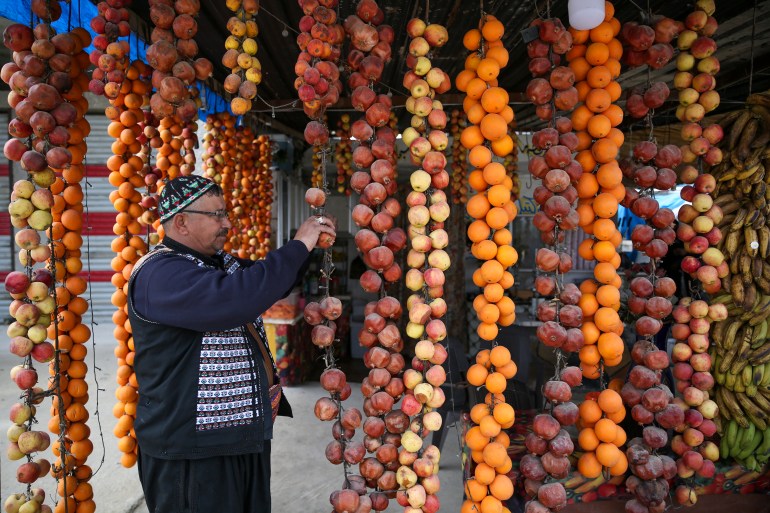 Idlib's Juice King, Safwan Daaboul, picks dried pomegranate off strings of fruit in front of his shop