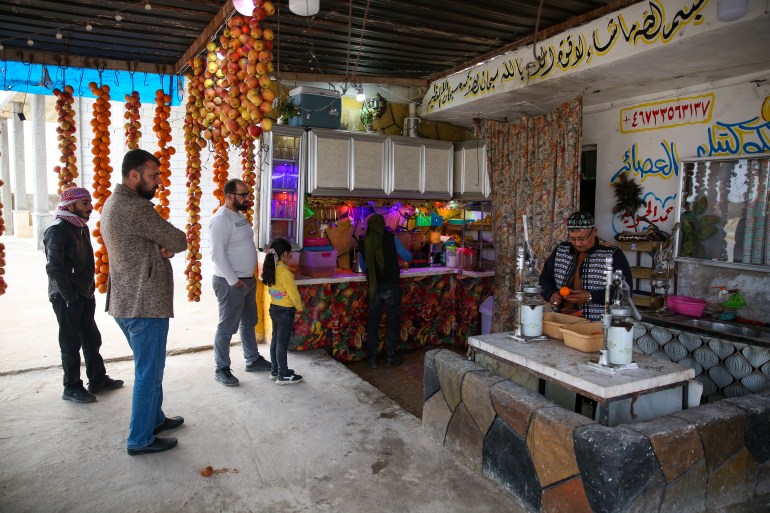 Daaboul is making orange juice behind a counter while four customers wait beneath garlands of drying fruit for their drinks