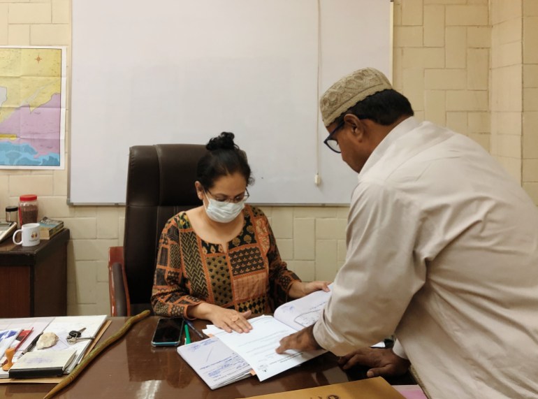 A photo of Dr Summaiya behind her desk examining a piece of paper someone is holding in front of her.