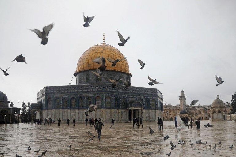 Palestinians walk next to the Dome of the Rock Mosque in the Al Aqsa Mosque