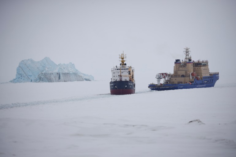 An Icebreaker making the path for a cargo ship with an iceberg in the background near a port on the Alexandra Land island near Nagurskoye, Russia, Monday, May 17, 2021. 