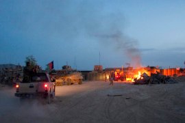 an Afghan National Army pickup truck passes parked U.S. armored military vehicles, as smoke rises from a fire in a trash burn pit at Forward Operating Base Caferetta Nawzad, Helmand province south of Kabul, Afghanistan.