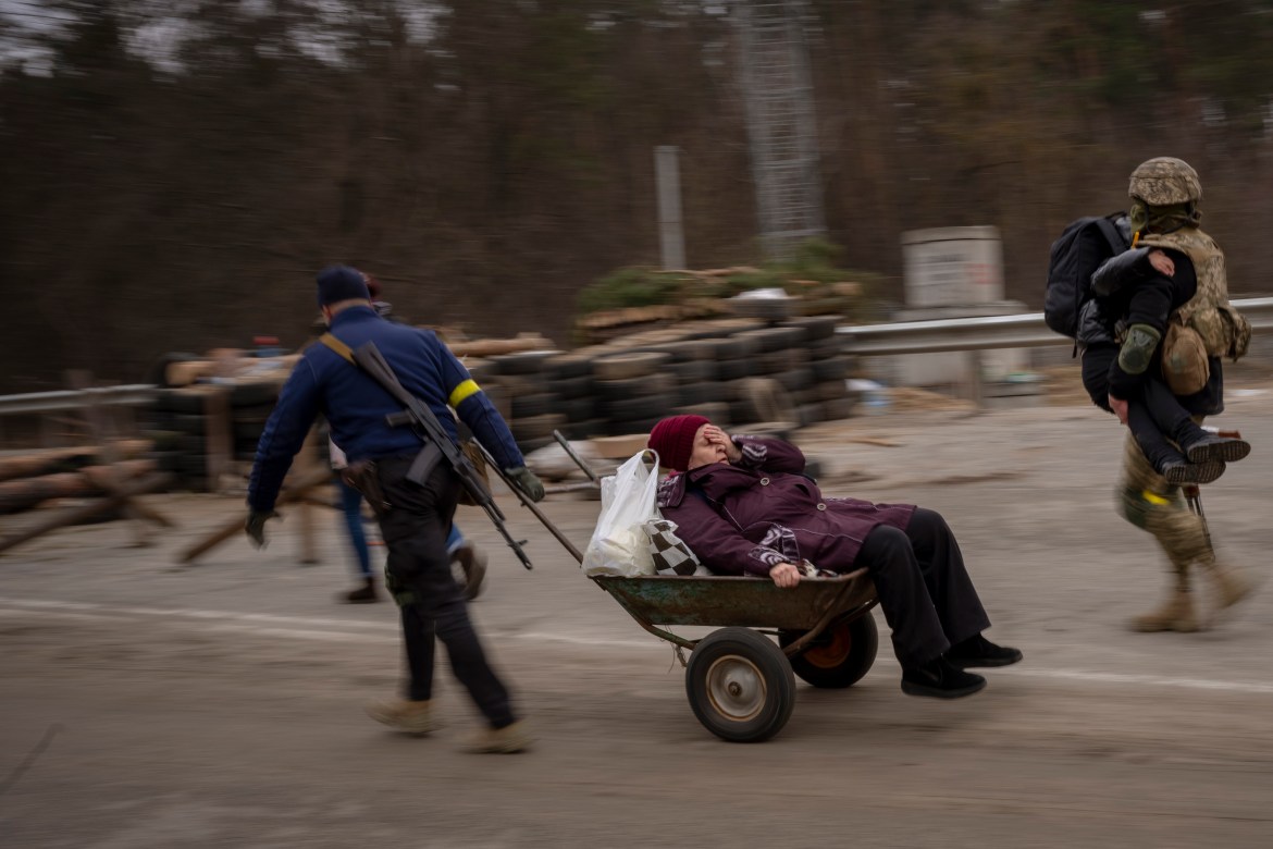 A Ukrainian soldier and a militia man help a fleeing family crossing the Irpin River in the outskirts of Kyiv
