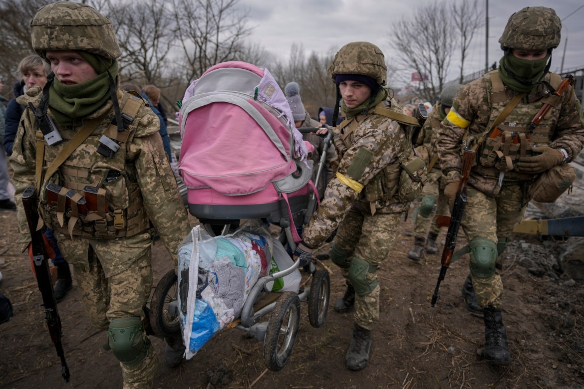 Ukrainian servicemen carry a baby stroller after crossing the Irpin River on an improvised path under a bridge that was destroyed by a Russian airstrike
