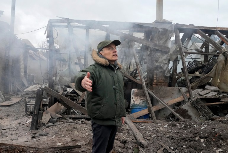 Un hombre abre los brazos mientras está de pie cerca de una casa destruida por el fuego de artillería ruso en Ucrania.