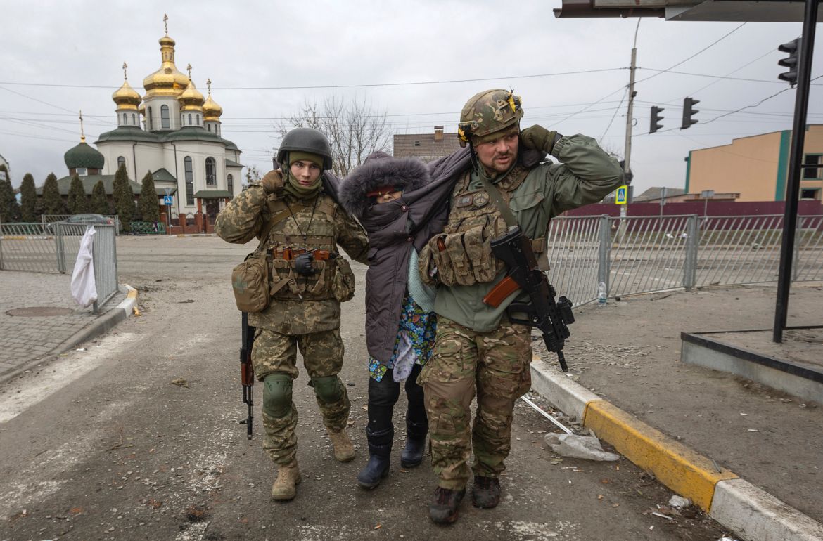 Ukrainian servicemen help an elderly woman, in the town of Irpin