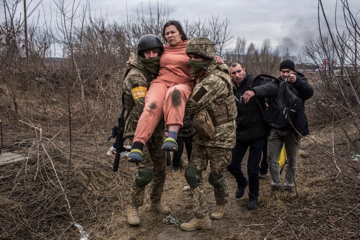 A woman carried by Ukrainian soldiers crosses an improvised path while fleeing the town of Irpin