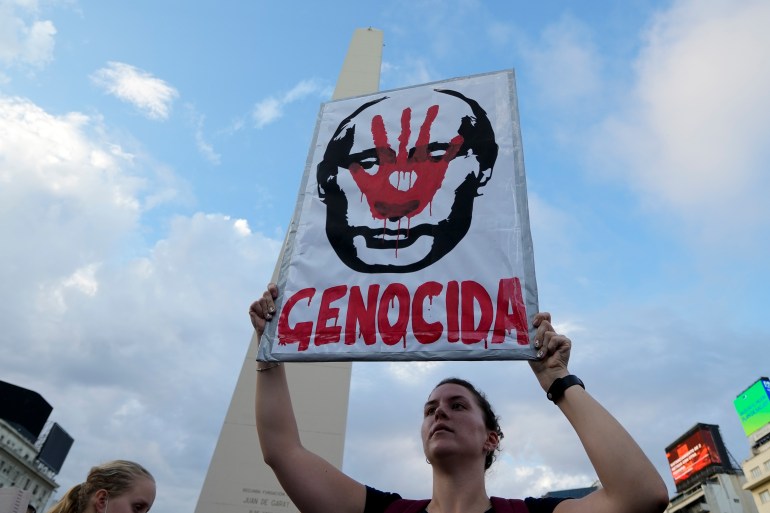 A woman holds a sign with the face of Putin and the word 'Genocidal' written in Spanish during a rally in Buenos Aires, Argentina