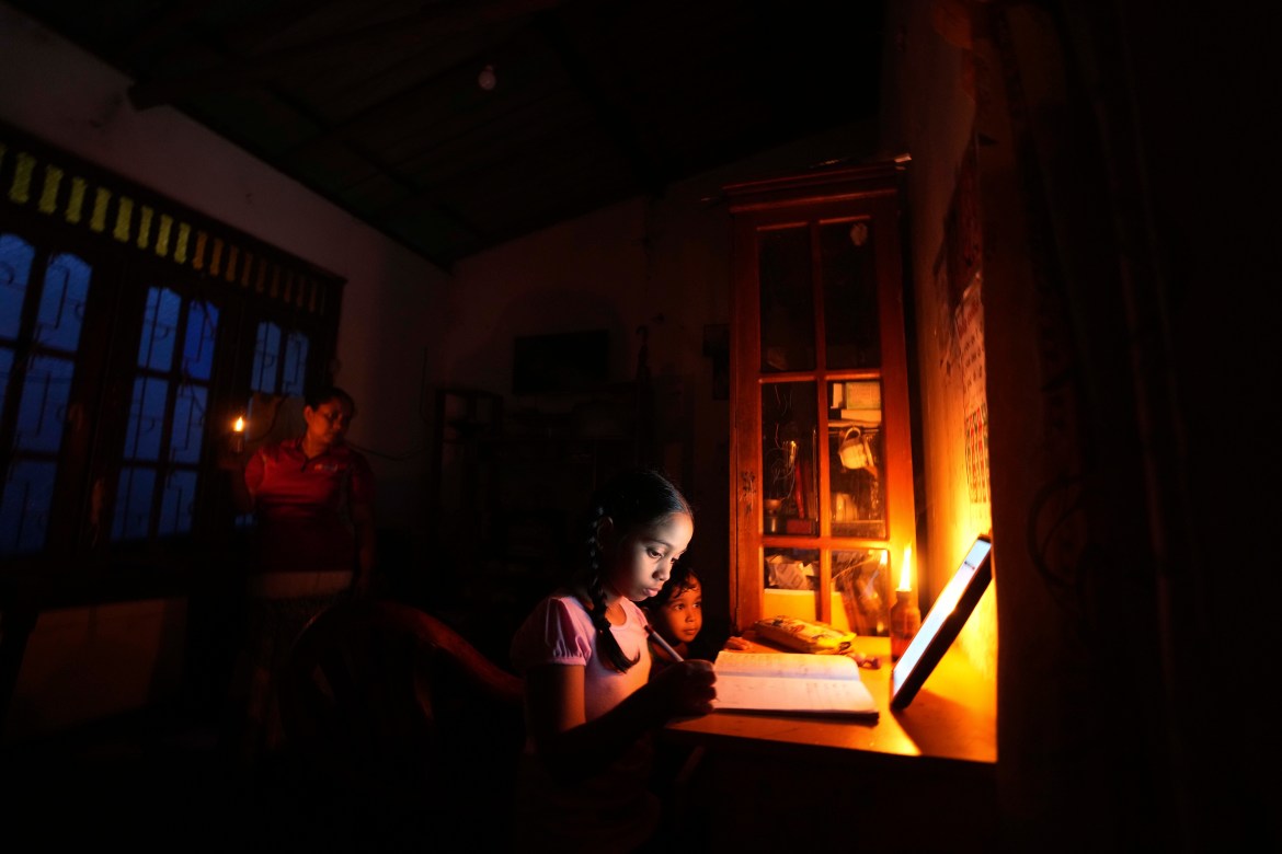 Children using kerosene oil lamps to study during long power outages in Colombo.