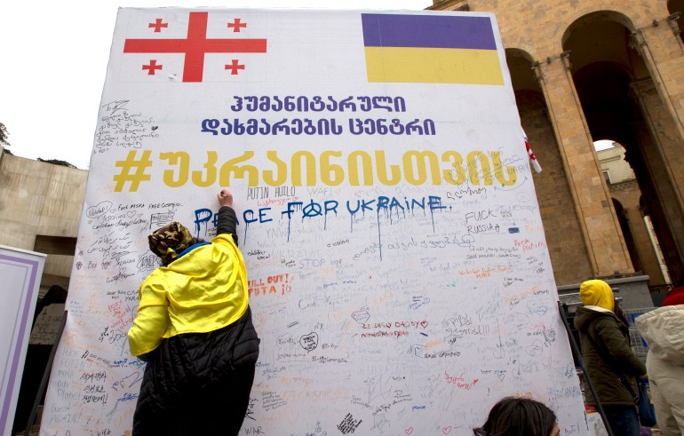 A woman writes words in support of Ukraine on a wall in Georgia