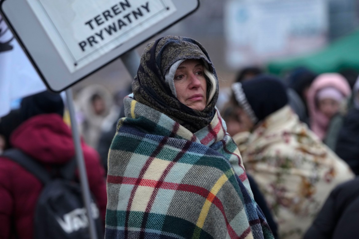 A woman wraps herself in a blanket to keep warm as she waits in a crowd of refugees after fleeing from Ukraine