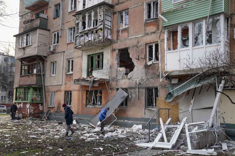 People walk next to an apartment building hit by shelling in Mariupol,