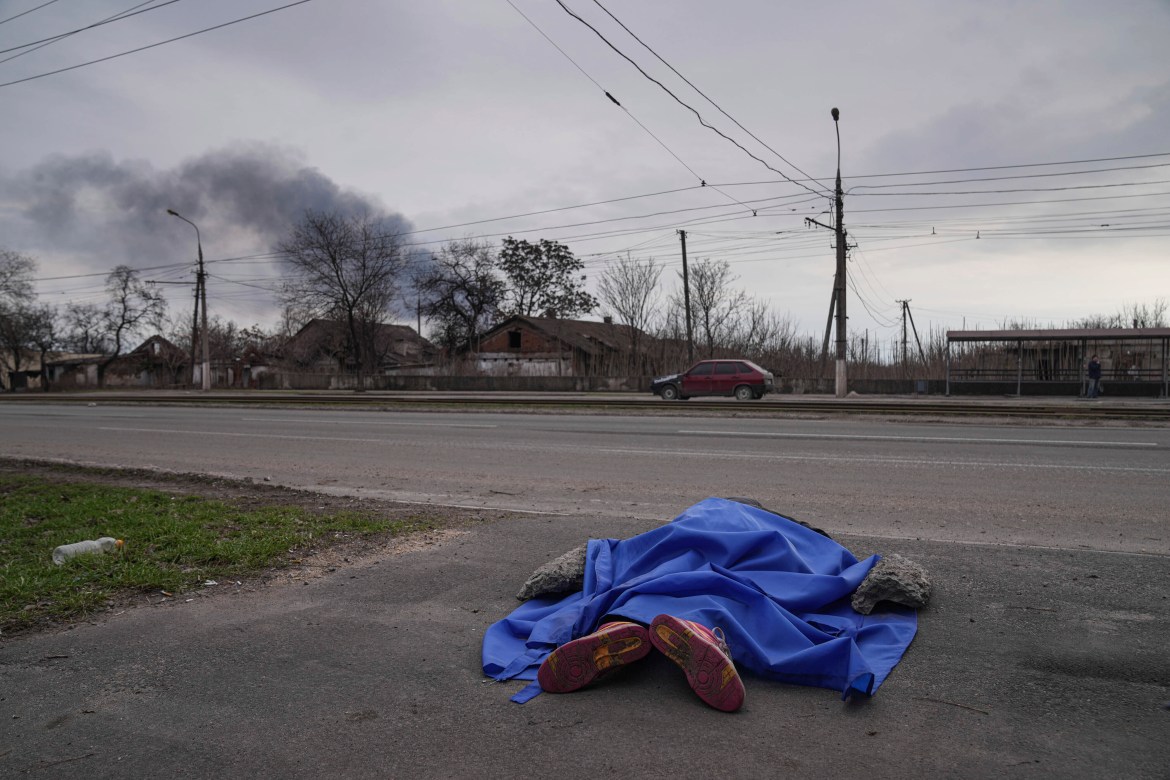 The dead body of a person lies covered in the street in Mariupol,