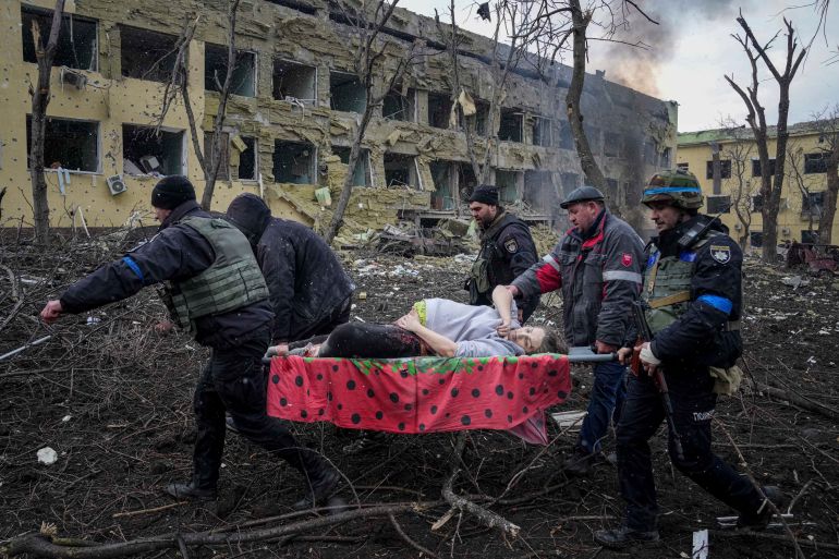 Ukrainian emergency employees and volunteers carry an injured pregnant woman