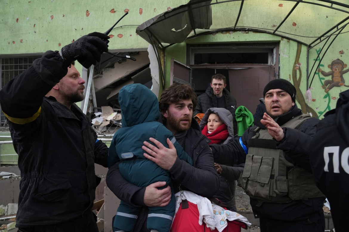 A man carries his child away from the damaged by shelling maternity hospital in Mariupol