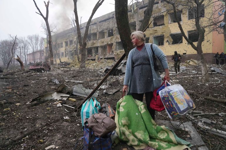 Una mujer pasa junto a un hospital de maternidad dañado por una bomba en Mariupol. [Evgeniy Maloletka/AP]