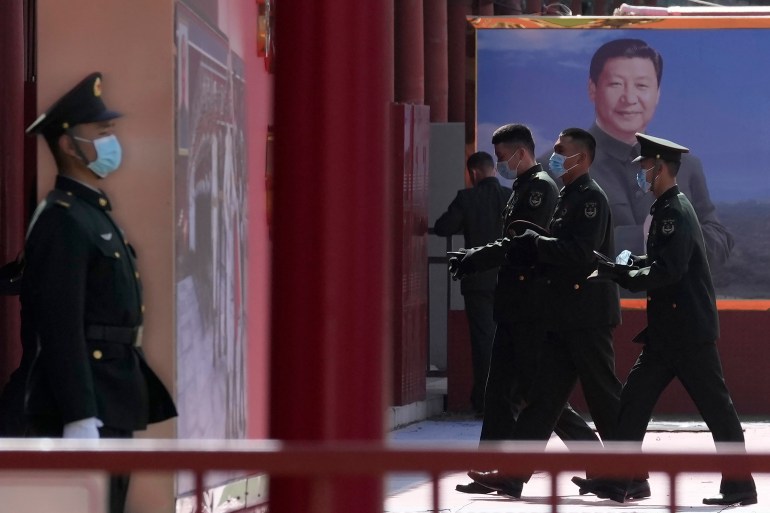 A photo of Chinese military personnel pass by a board displaying a photo of Chinese President Xi Jinping.
