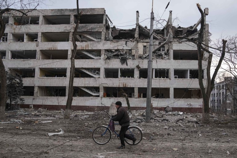 A man walks with a bicycle in front of a damaged by shelling in Mariupol, Ukraine