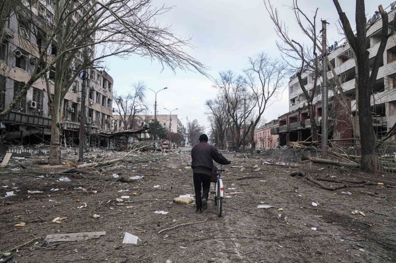 Un hombre camina con una bicicleta en una calle dañada por los bombardeos en Mariupol, Ucrania