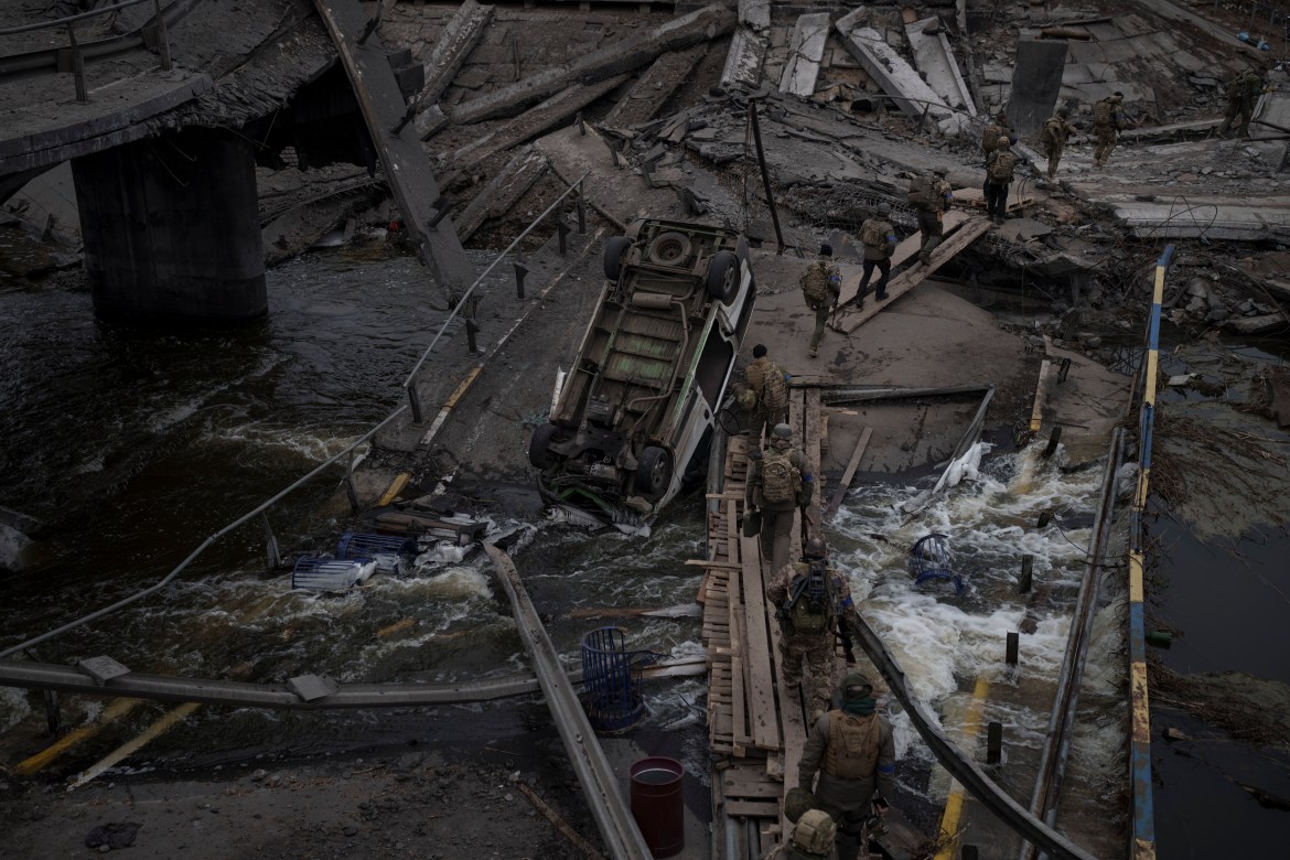 Foreign and Ukrainian soldiers cross an improvised path under a destroyed bridge in Irpin, outskirts of Kyiv