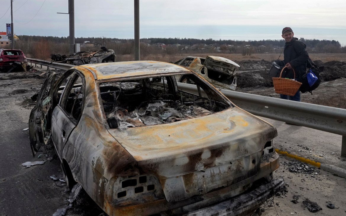 A resident passes by cars burnt in the Russian shellfire as he flees from his hometown on the road towards Kyiv