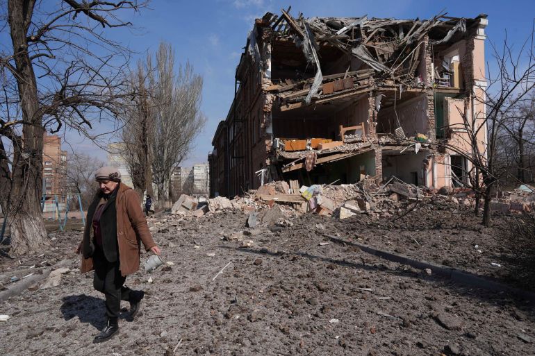 A woman walks past building damaged by shelling in Mariupol, Ukraine