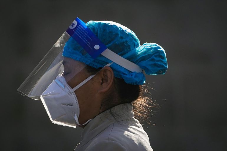 A close up of a woman in personal protective equipment including head covering, N95 mask and face shield