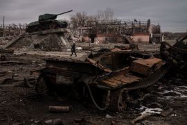 A woman walks past a destroyed tank in the town of Trostsyanets, Ukraine