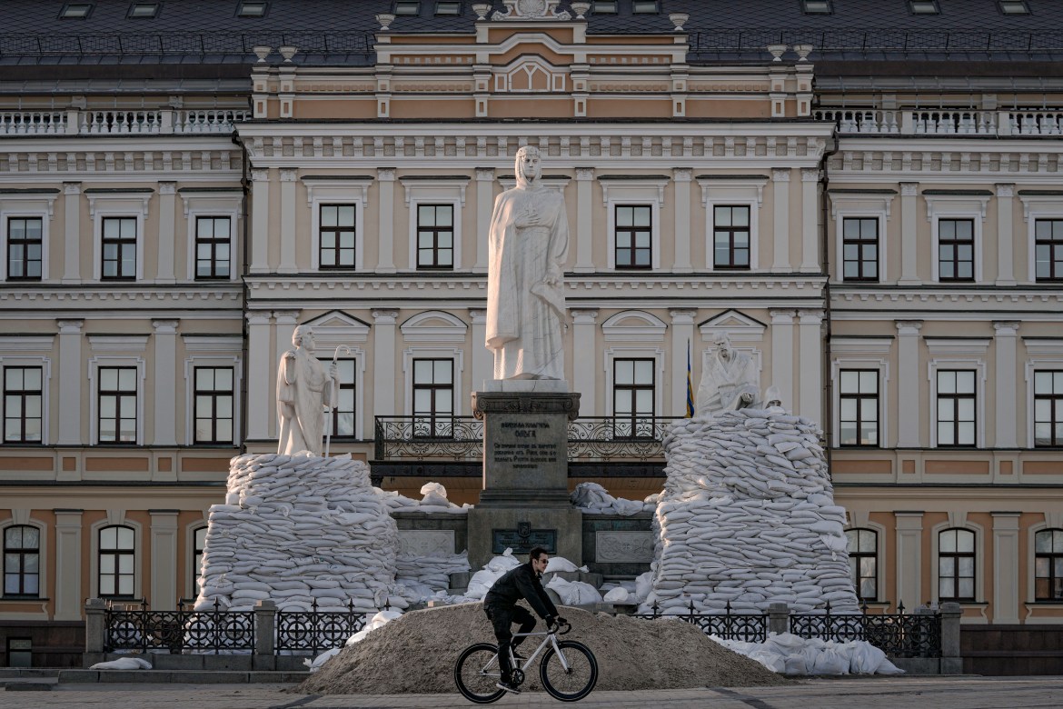 A man rides a bicycle backdropped by a statue of Grand Princess Olga of Kyiv