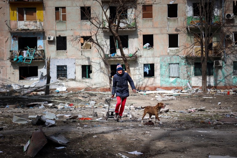 A man walks with his dog near an apartment building damaged by shelling from fighting on the outskirts of Mariupol