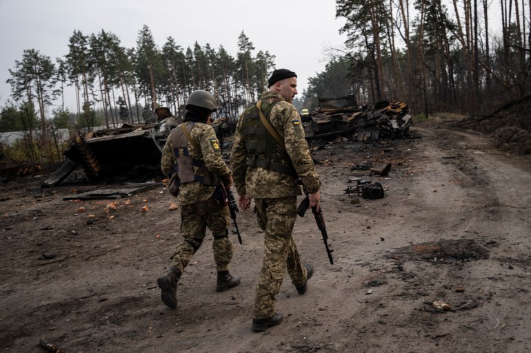 Ukrainian soldiers walking past a destroyed Russian tank