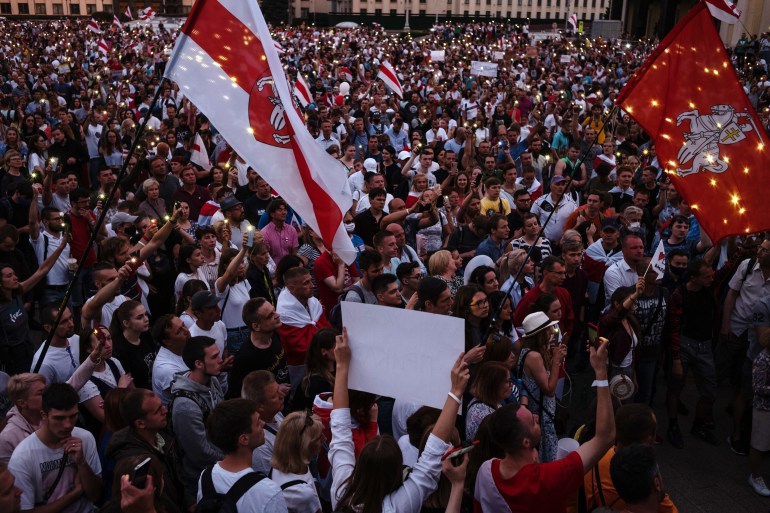 A photograph  of a ample  radical  of radical   astatine  a rally holding Belarus flags and signs.