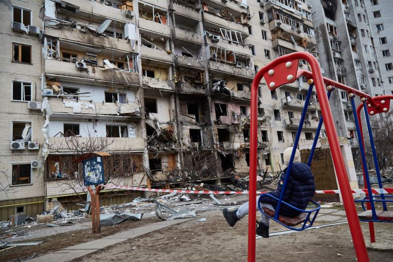 A child is seen on a swing in front of a residential building damaged by shelling in Kyiv