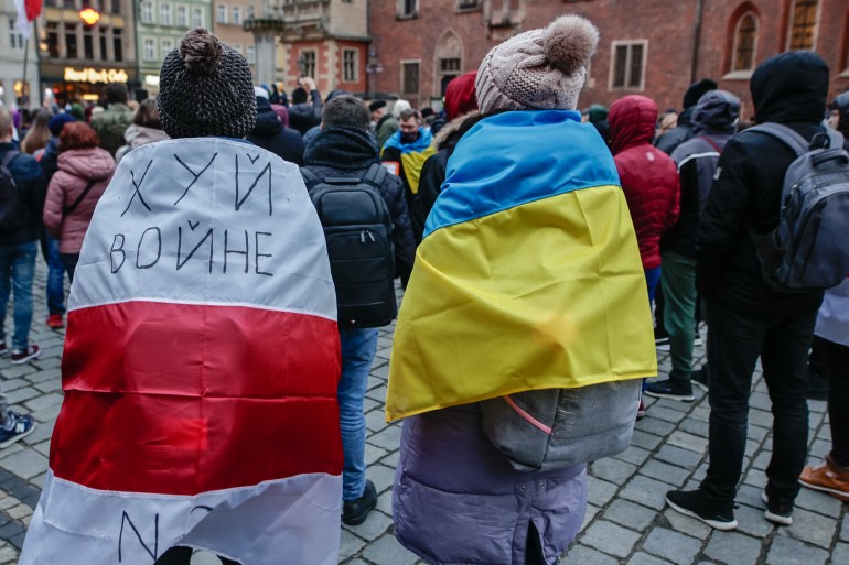 A photo of two people wearing flags, the one on the right is wearing the Polish flag and the other is wearing the Ukrainian flag.