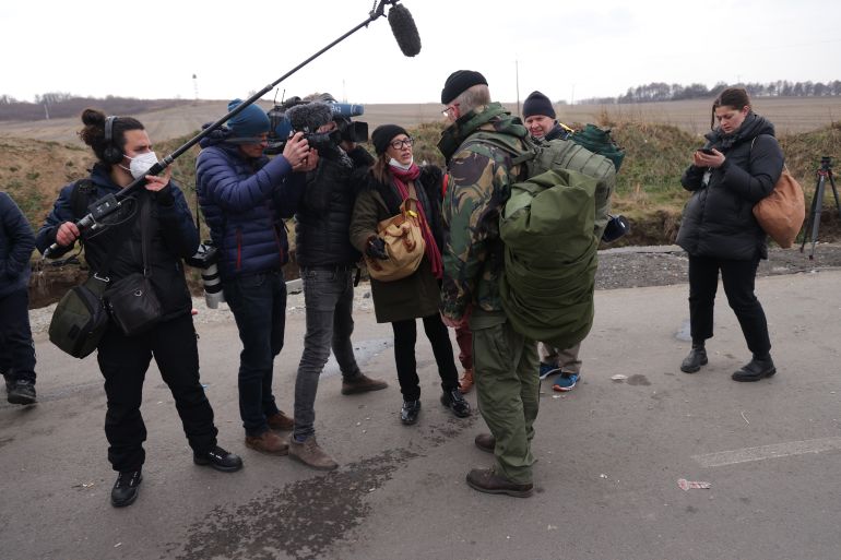 Members of the media interviewing a man in military fatigues.
