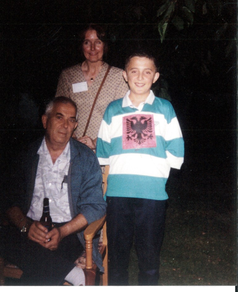 Una foto de tres personas, un hombre sentado en una silla, una mujer detrás de él y Hasan Rrahmani de niño junto a ellos.