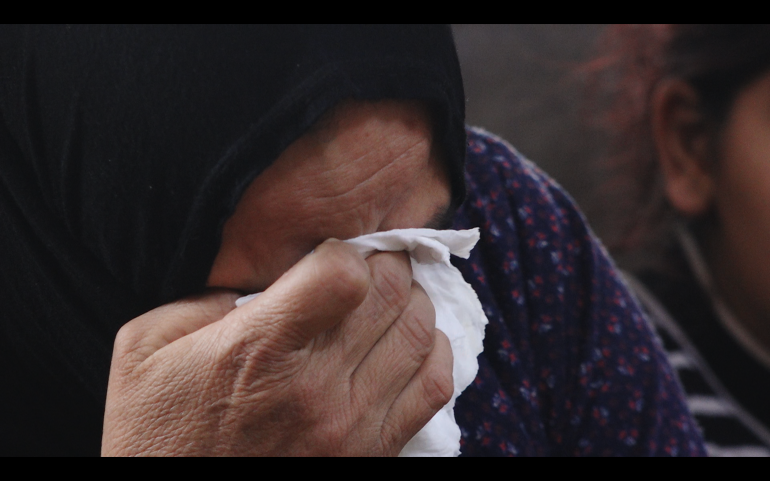A woman wearing a black headscarf crying in a tissue