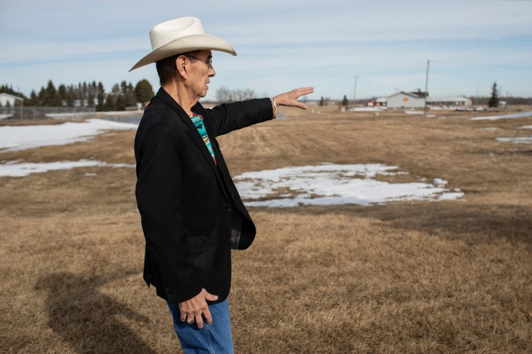 A photo of Chief Willie Littlechild pointing towards the distance in a field.