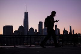 Buildings stand in the lower Manhattan skyline as a pedestrian walks along the Hudson River Waterfront Walkway in Jersey City, New Jersey, U.S.