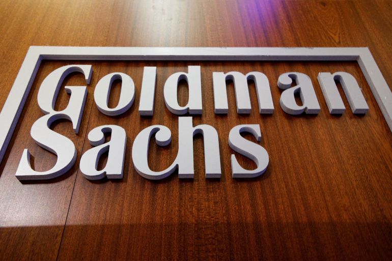 Goldman Sachs logo on a wood-panelled wall.