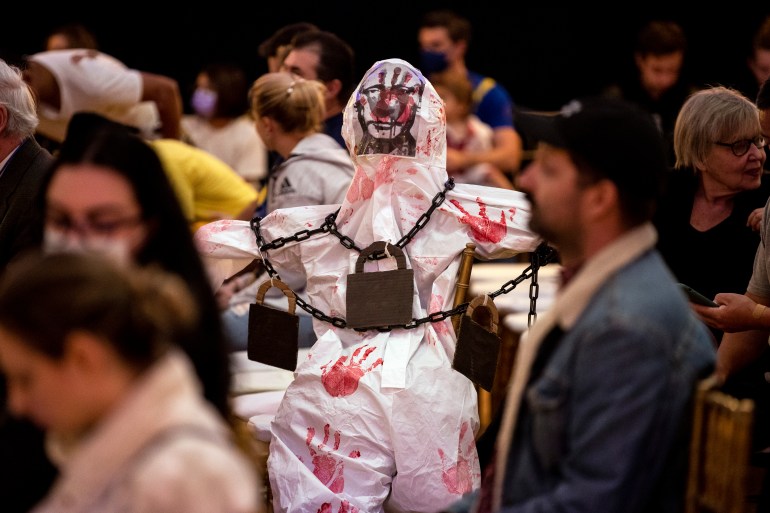 A bloodied mannequin displaying the face of Vladimir Putin sits amid the audience during a meeting